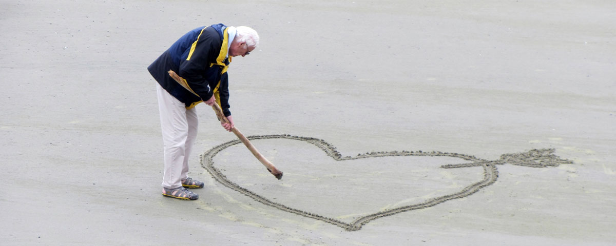 Elderly man drawing a heart in the sand