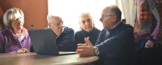 A group of four older people sitting around a table with a laptop.